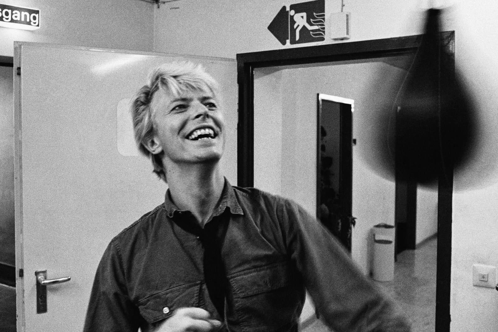 David Bowie laughs backstage while playfully striking a speed bag in candid black-and-white photograph during tour break.