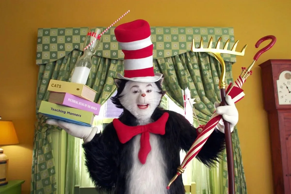 Mike Myers as the Cat in the Hat balances books, milk, umbrella, and garden rake indoors.