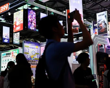 A silhouetted visitor photographs colourful gaming posters and screens at an expo.