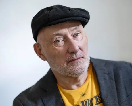 The musician Jah Wobble wearing a flat cap, blazer and T-shirt
