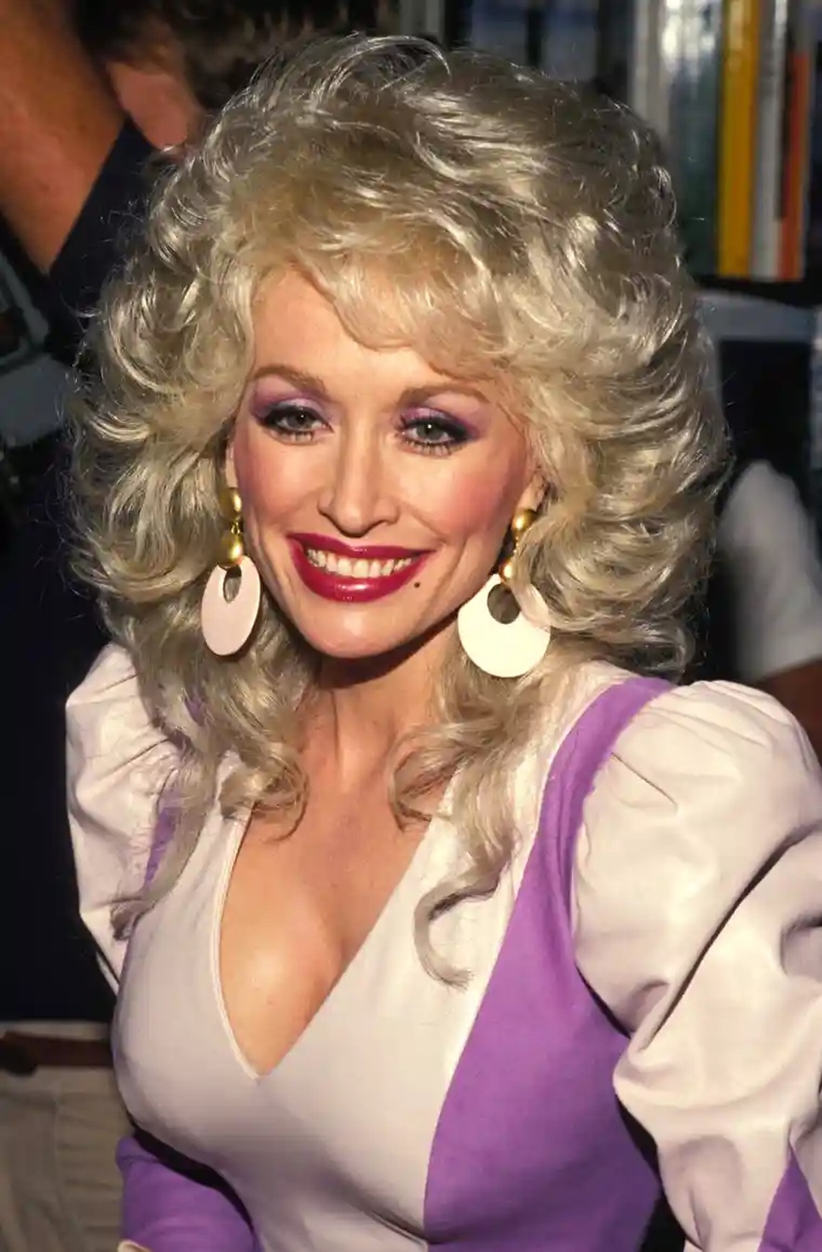 A woman smiling while wearing a pale pink and purple top with puffy shoulder sleeves