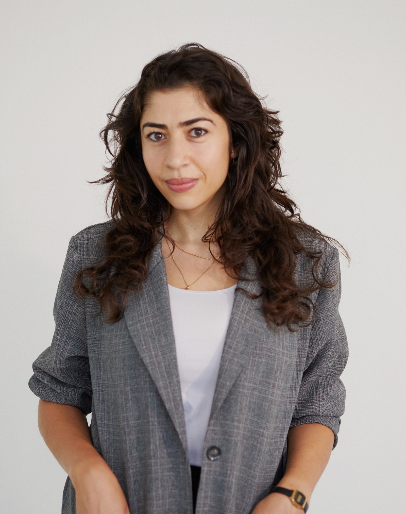 a woman wearing a grey blazer poses for the camera against a plain, grey background