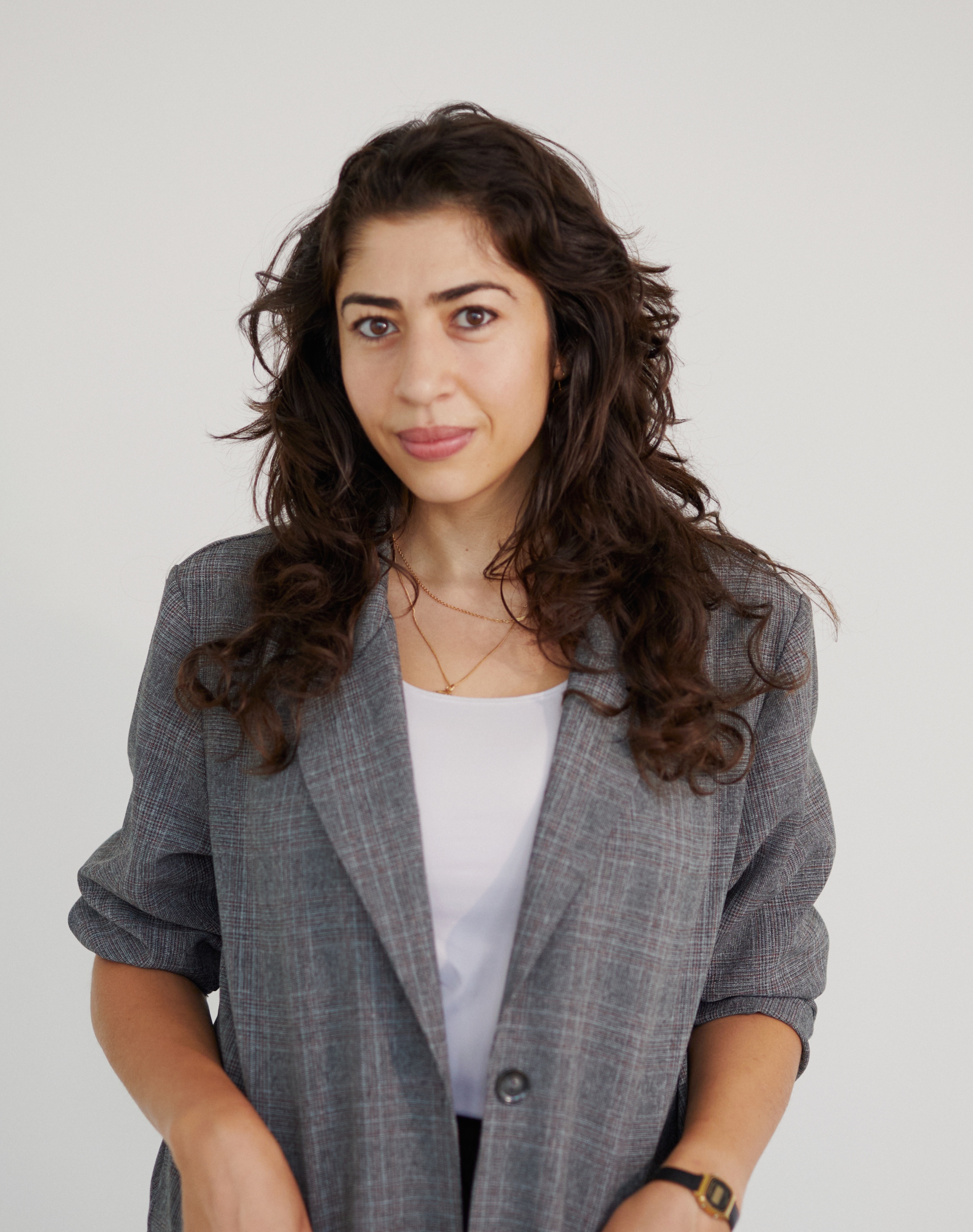 a woman wearing a grey blazer poses for the camera against a plain, grey background