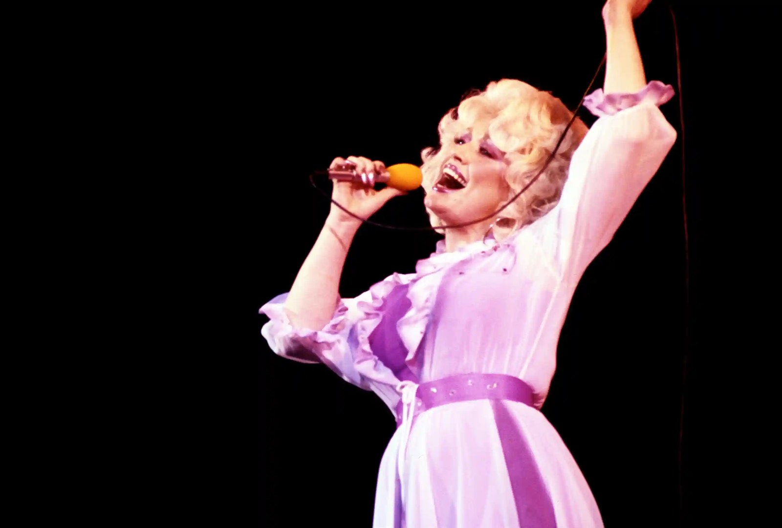 A woman wearing a pink frilly dress sings into a microphone