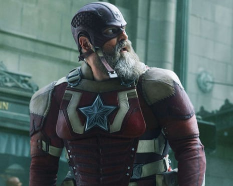 David Harbour, bearded, wears a worn leather Red Guardian costume and helmet, looking aside