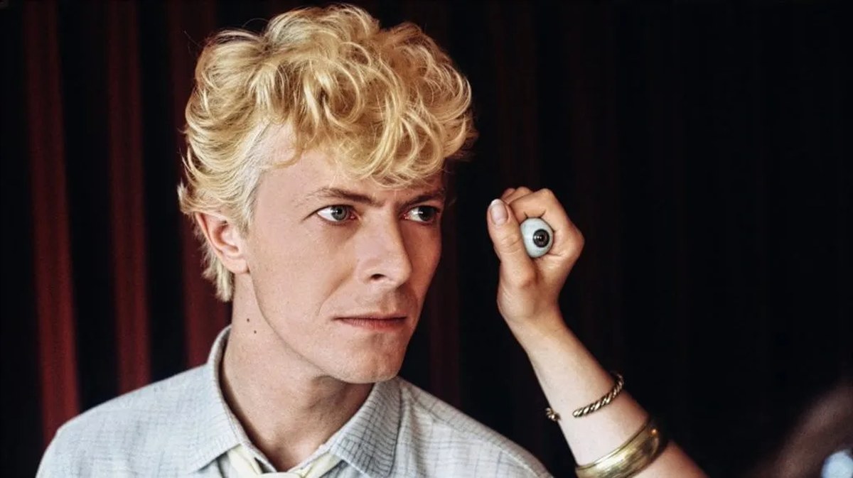 In a photo by Denis O'Regan, David Bowie receives makeup touch-up as an artist holds a realistic prosthetic eyeball beside his face