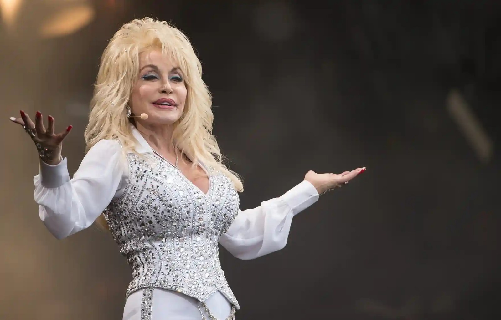 A woman performs on stage wearing a bedazzled white jumpsuit