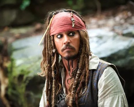 Johnny Depp as Captain Jack Sparrow, in braids and red bandana, looks sideways warily