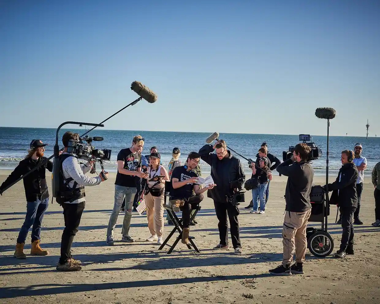 Frith on set on a beach surrounded by camera and microphone operators