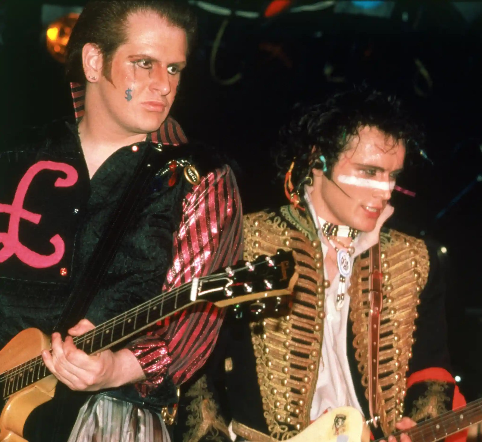 Adam and the Ants members in flamboyant costumes and face paint play electric guitars on stage