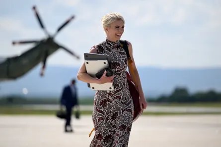 a woman smiles while holding a laptop outside