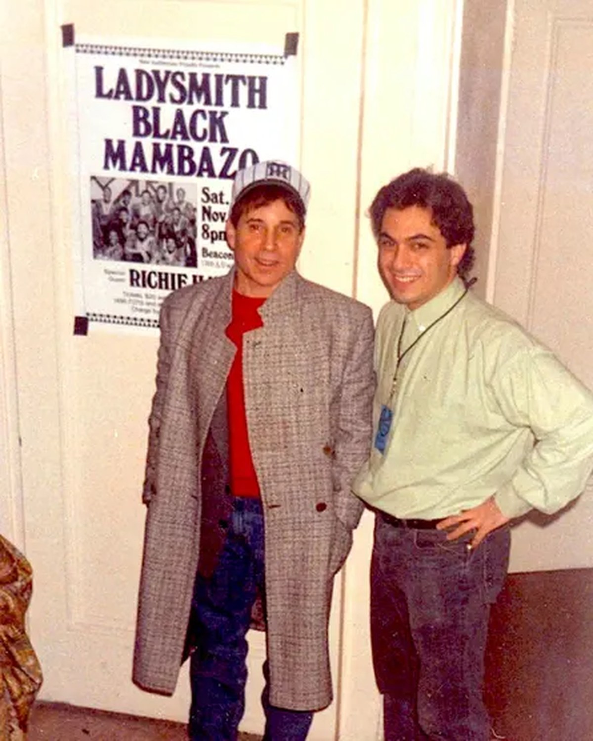 Two men smile in front of a poster for Ladysmith Black Mambazo