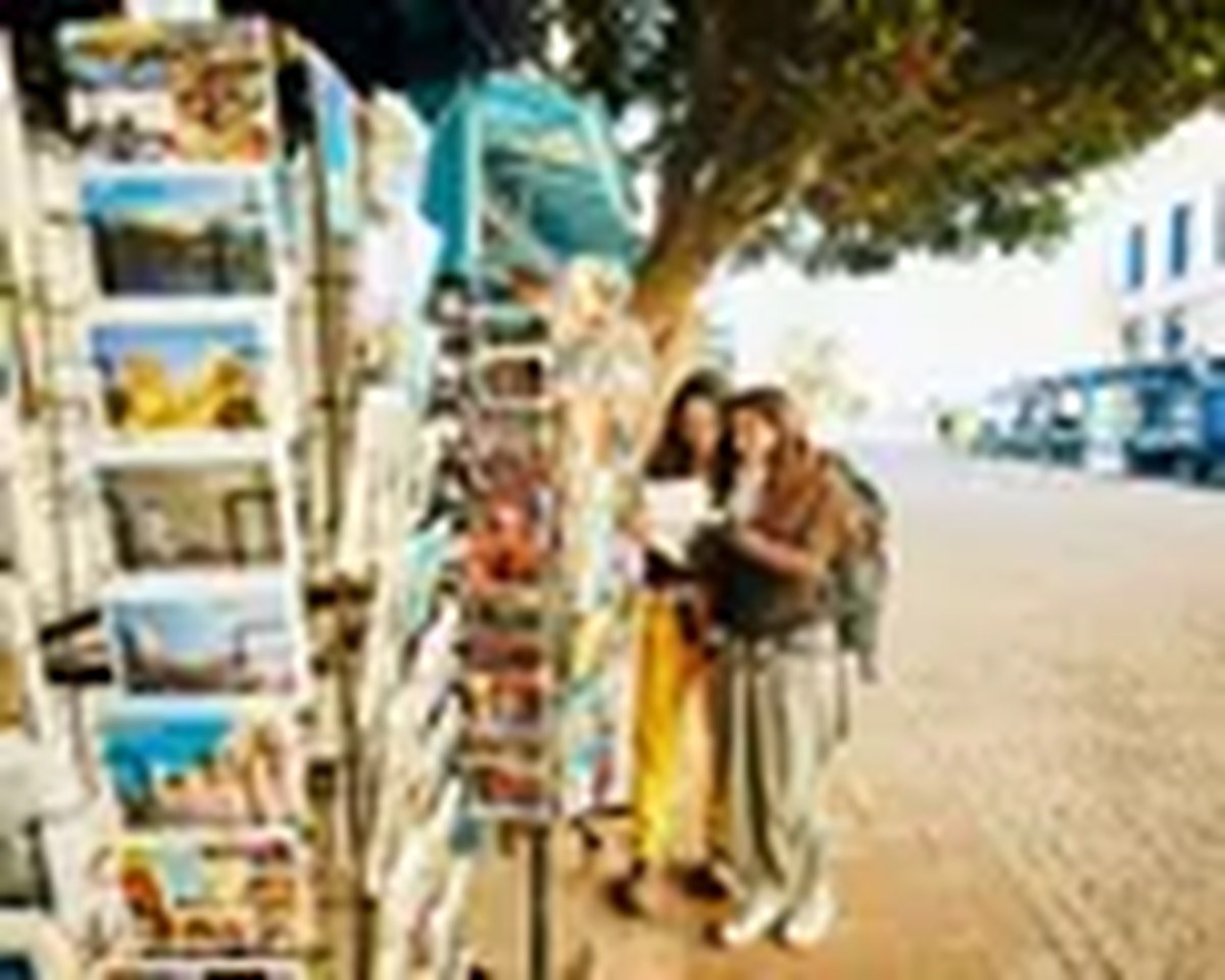 Wide shot sisters browsing through postcards at vendor in EssaouiraWide shot of smiling adult sisters browsing through postcards at street vendor while exploring Essaouira during backpacking trip in Morocco