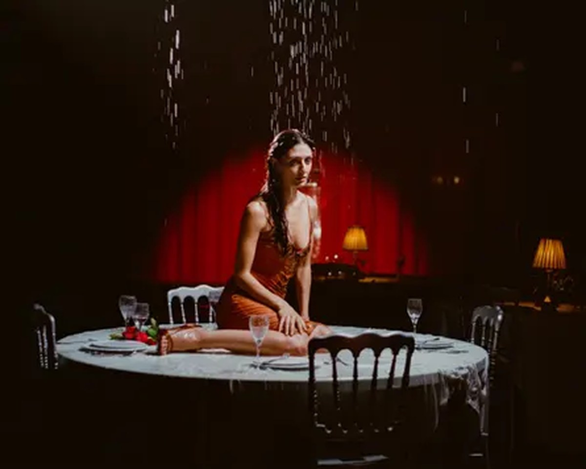 In a still from the video for Actress, Sofie Royer sits on a dining table as it rains from above