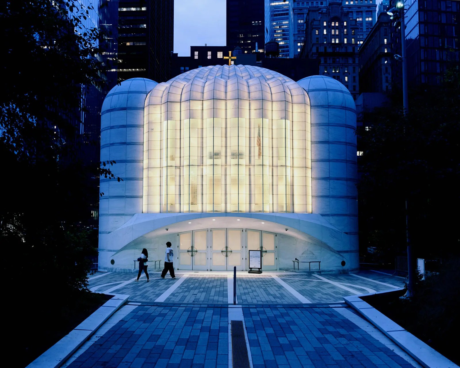 A man and a woman walk past a domed marble light box of a church.