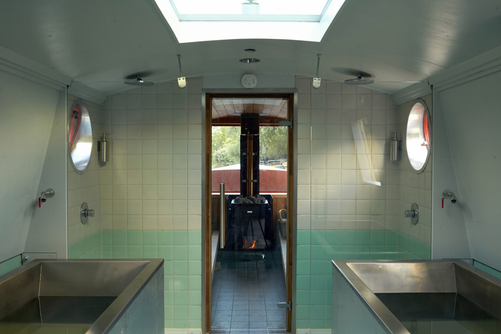 Two stainless-steel plunge pools in a pale green tiled room beneath a skylight