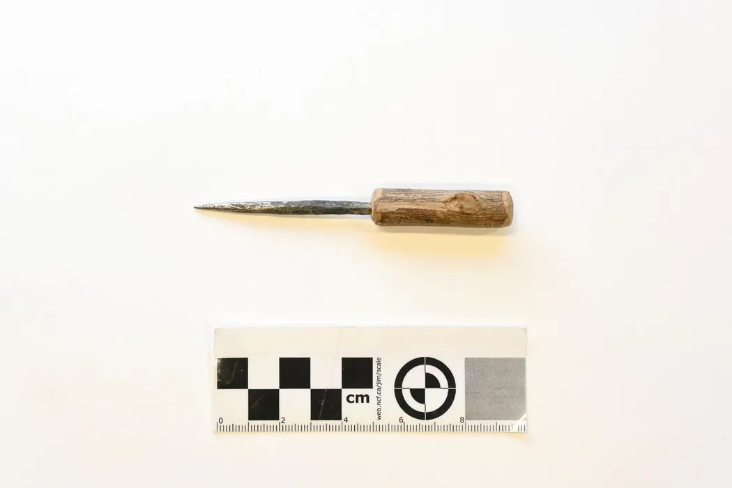 Small iron awl with a wooden handle of wood with bark remaining except where carved at the ends. The blade is firmly fastened in the handle. The blade is of iron which is squared off at handle and ground to a sharp point at the other end. - Bilinmiyor