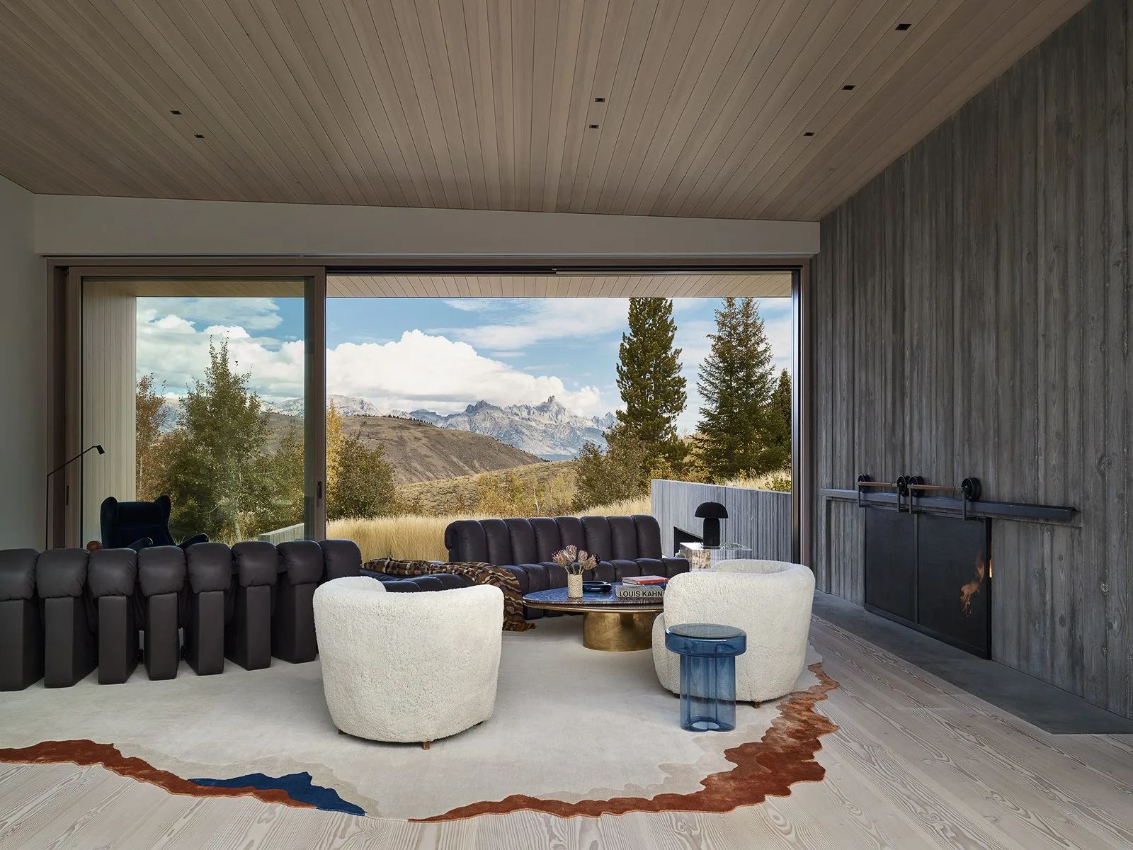 Living room with a dark sofa and two cream-colored armchairs facing a large window wall that overlooks a mountain landscape.