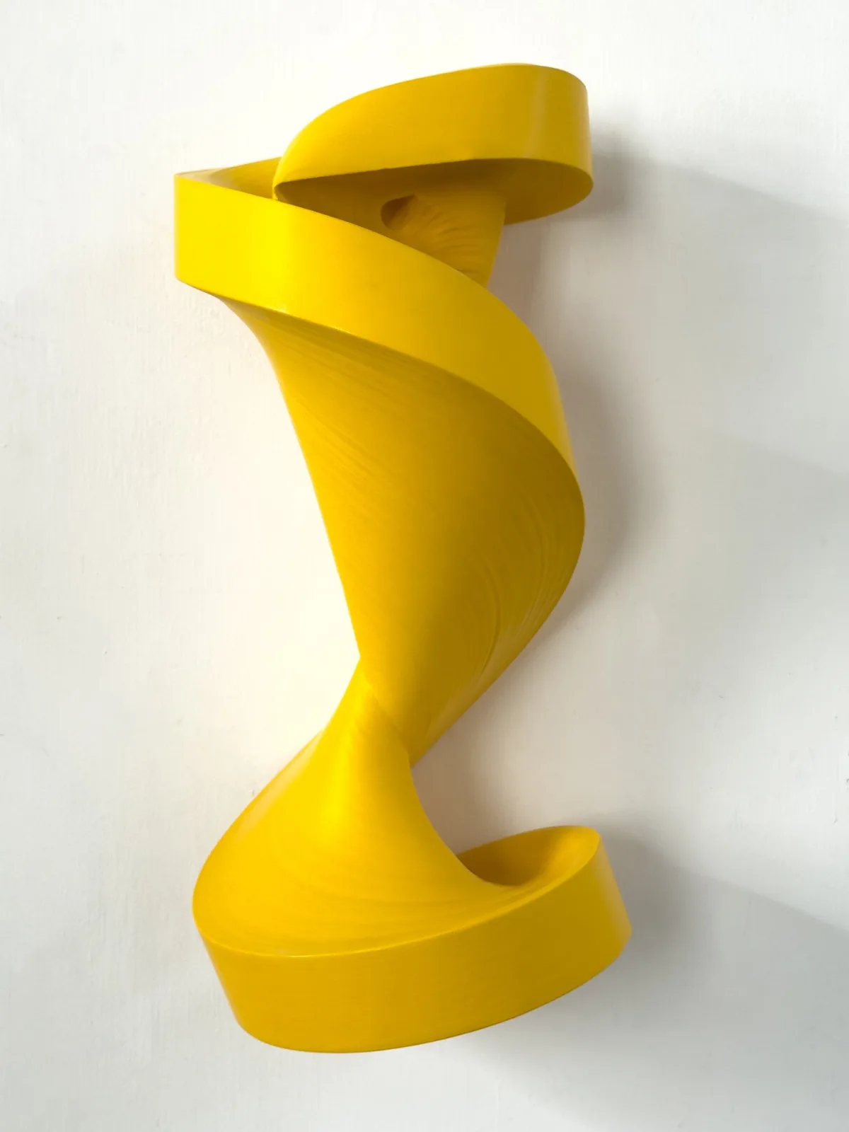 A yellow, spiral-shaped abstract wall sculpture in the style of Jae Ko.