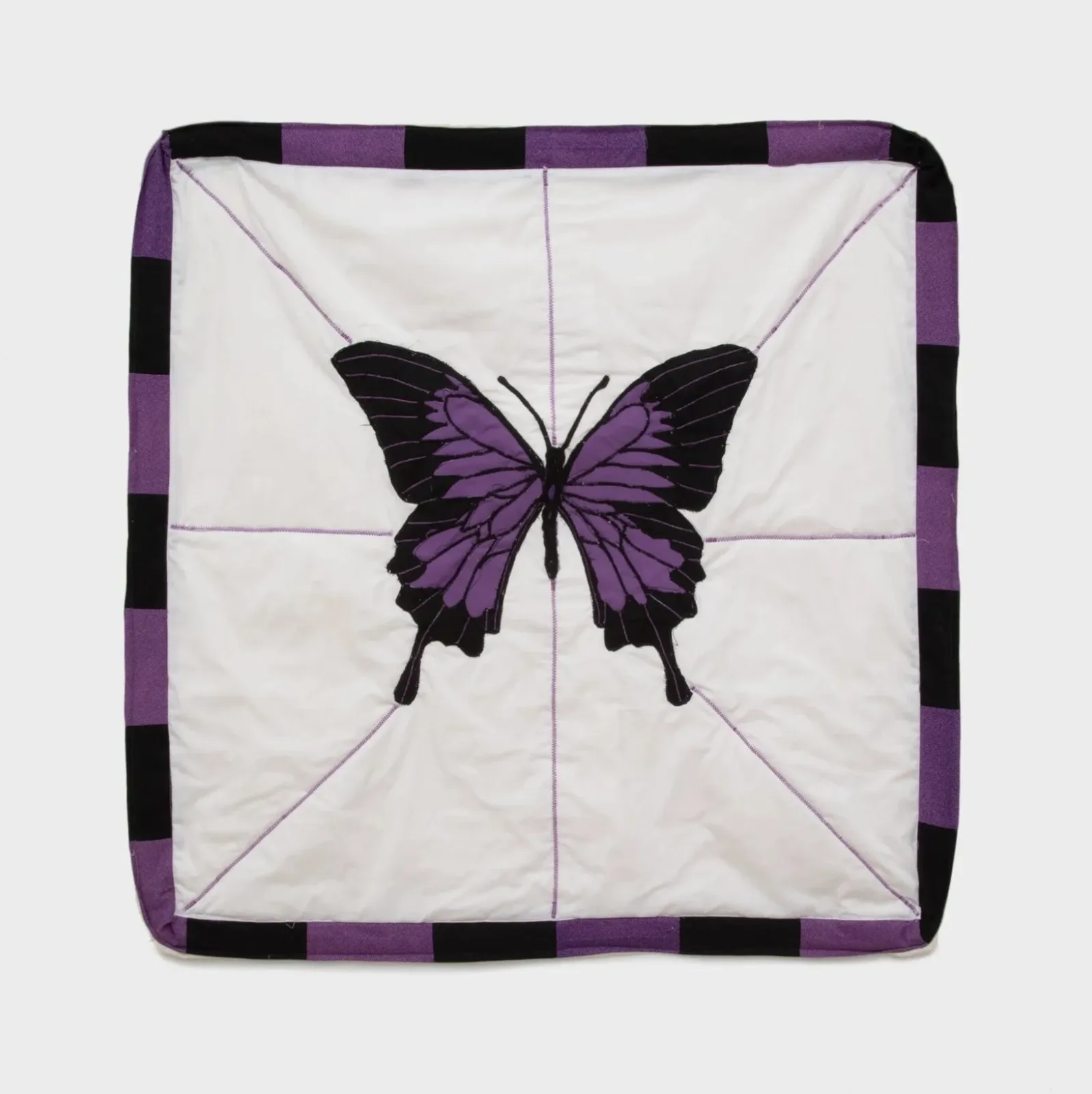 Quilted textile square featuring an appliquéd purple and black butterfly centered on white fabric with a checkered purple-black border.