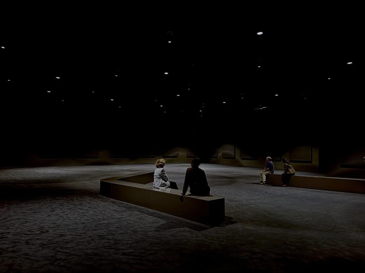 some benches are placed in the middle of a large darkened room, three people sit on them