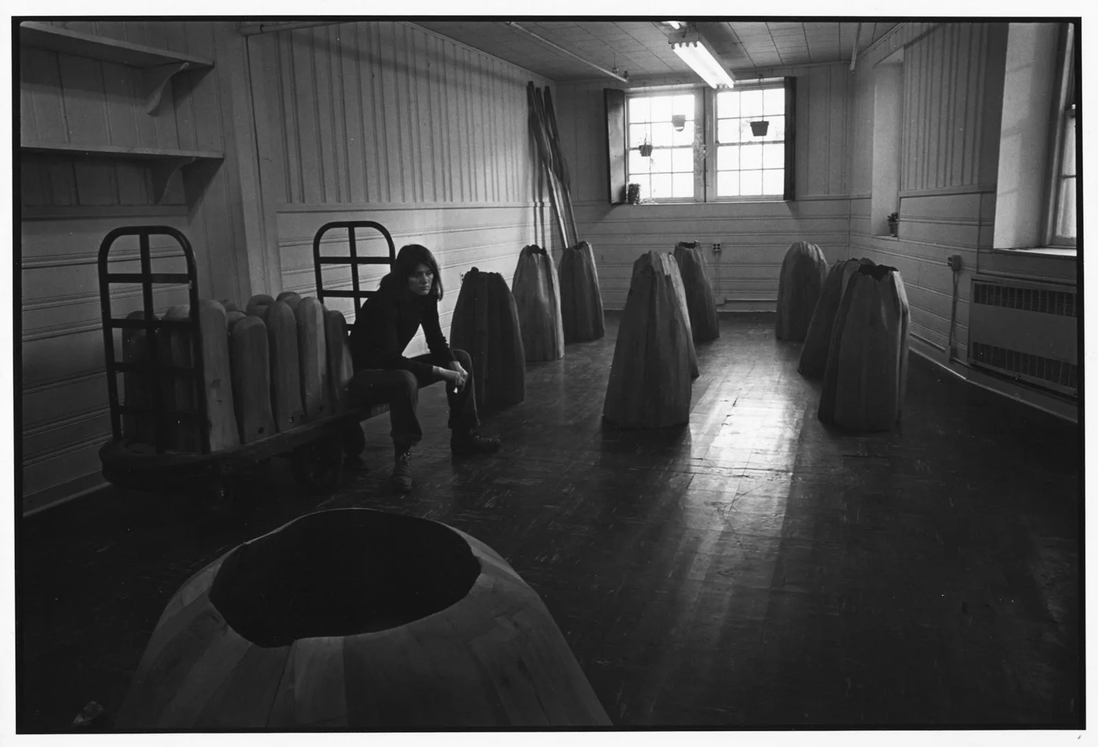a black and white photo of a woman in a studio with wooden sculptures around her