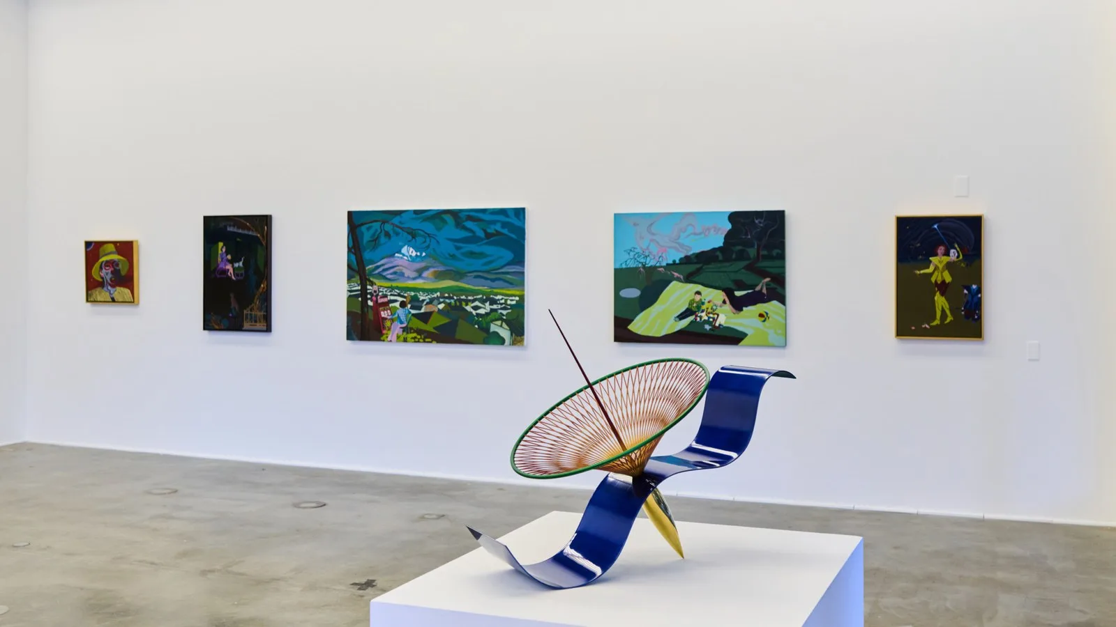 Five paintings hang on a white gallery wall behind a sculptural piece in a Veronica Mishaan Bogotá penthouse, featuring a blue curved base, a conical wire structure, and a thin central rod.
