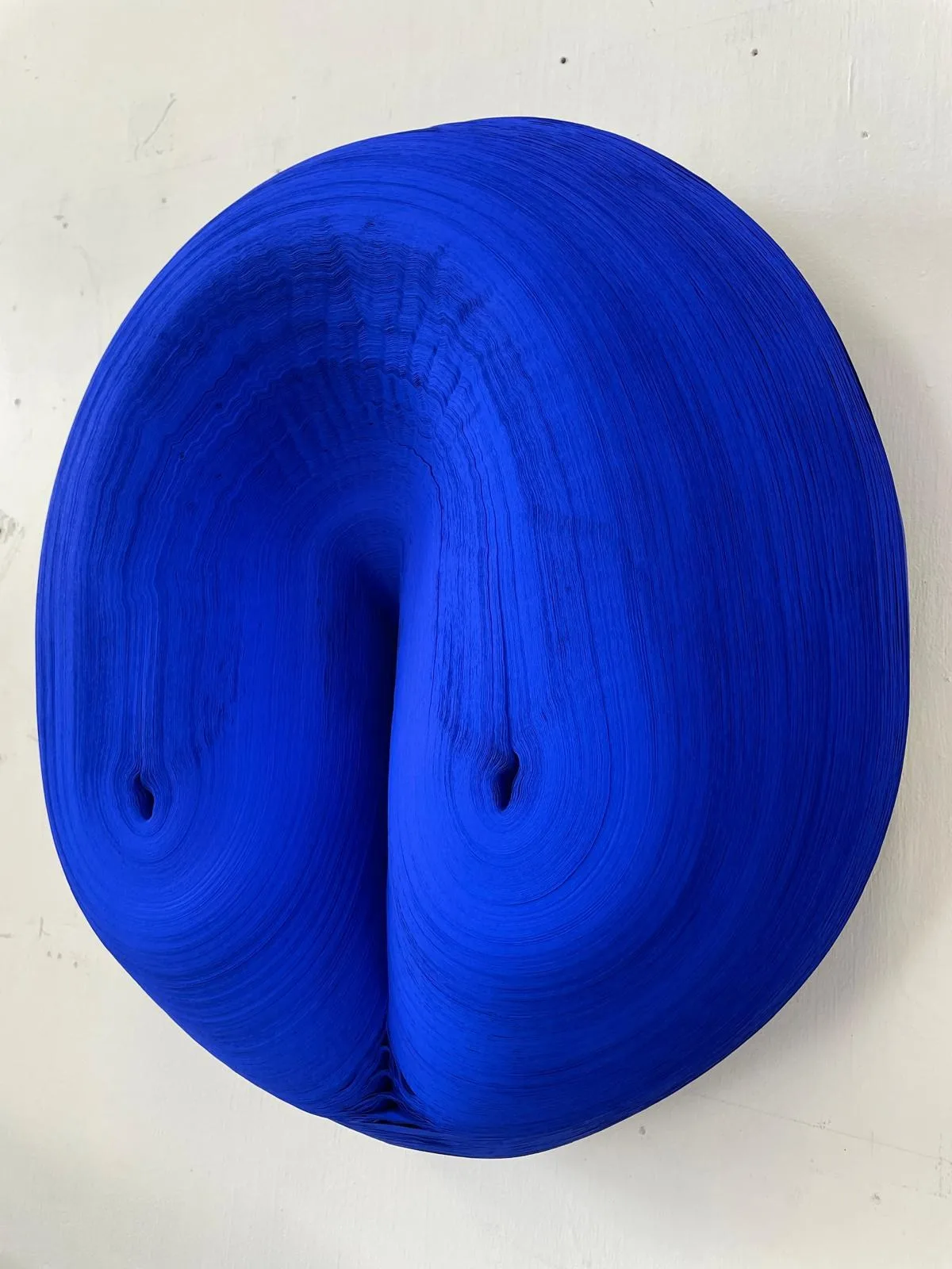 A circular, bright blue Jae Ko sculpture featuring a dense, layered texture with a central indentation.