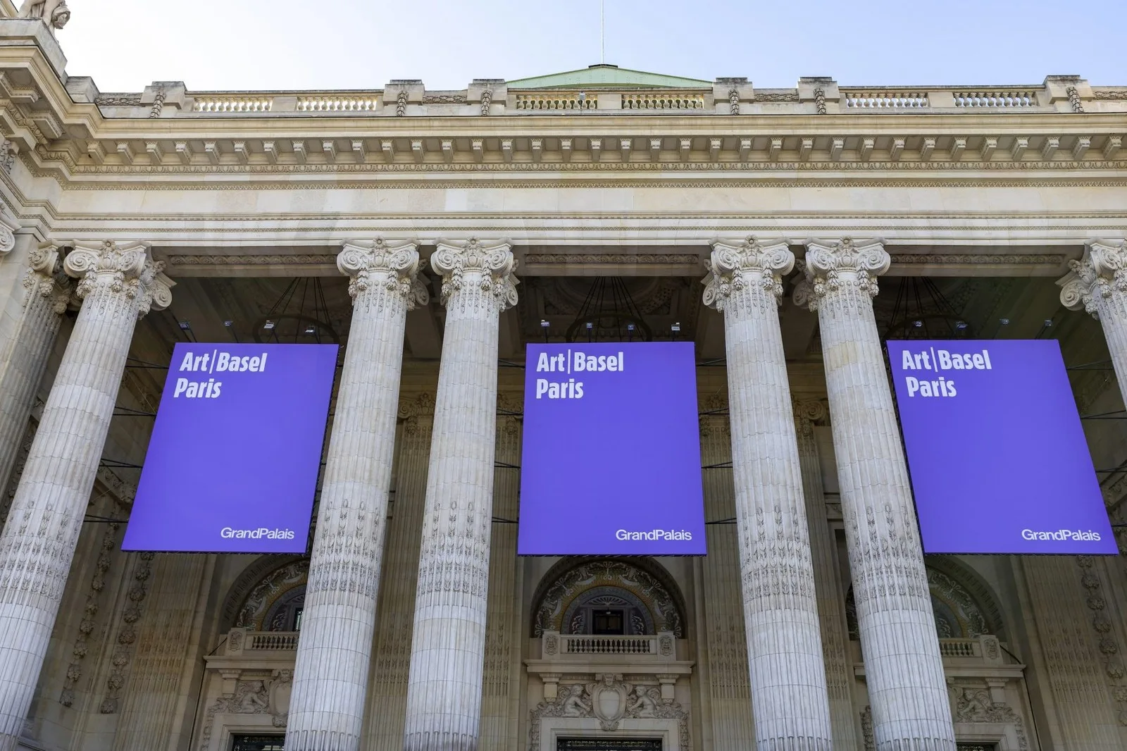 an upward look at columns on the front of a building with purples signage for Art Basel Paris