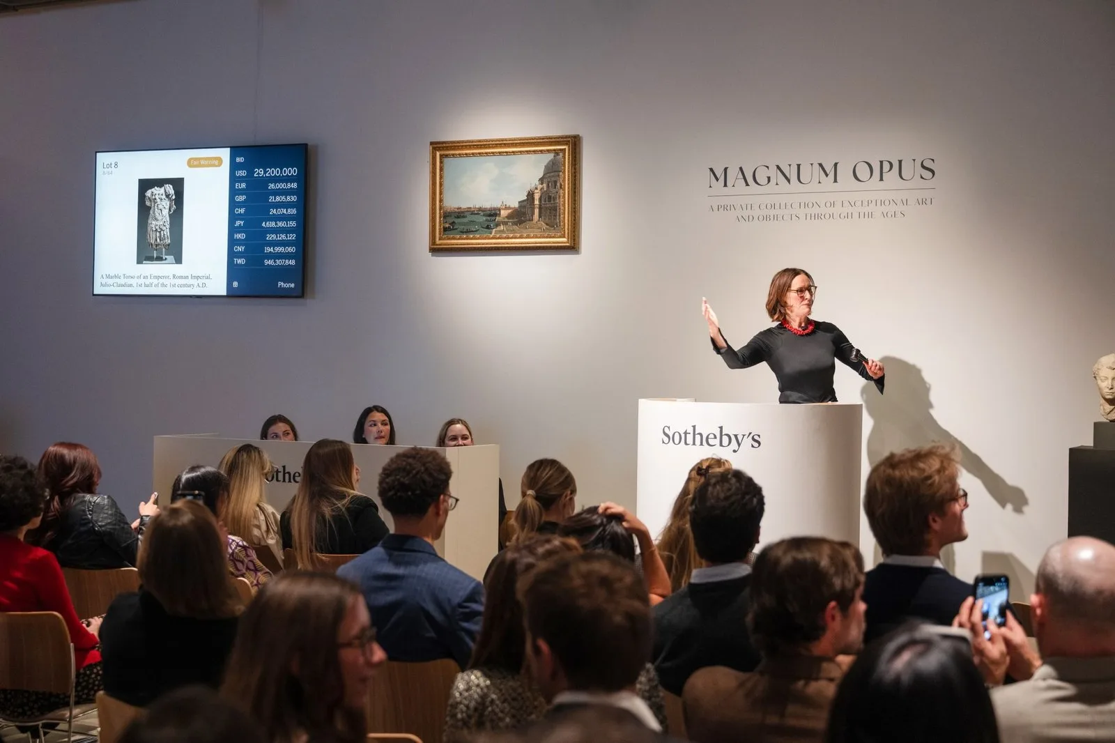 an auctioneer stands behind a white rostrum with a crowd in front